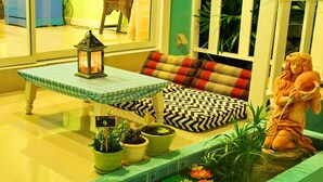 Una habitación acogedora con un banco a cuadros, una mesita con un farol, una estatua y plantas en macetas.