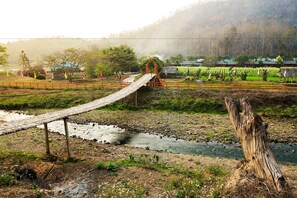 A rustic wooden bridge over a stream, surrounded by greenery and a misty background. - Karen Eco Lodge (Mae Wang)