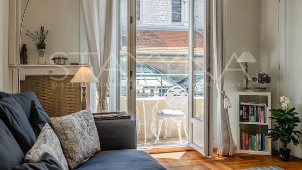 Ein modernes Wohnzimmer mit einer Couch, einem Bücherregal und Blick auf einen Innenhof durch eine Glastür.