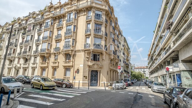 A multi-story building with ornate architectural details, a gated entrance, and a street view with parked cars.