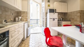A kitchen with white cabinets, a refrigerator, a stove, and a dining area with a red chair.