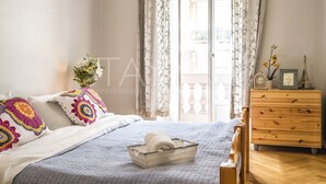 A bedroom with a bed, a wooden dresser, a window with curtains, and a view of the outside.