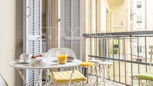 A balcony with a table set for breakfast, including a cup, saucer, teapot, and glass of orange juice.