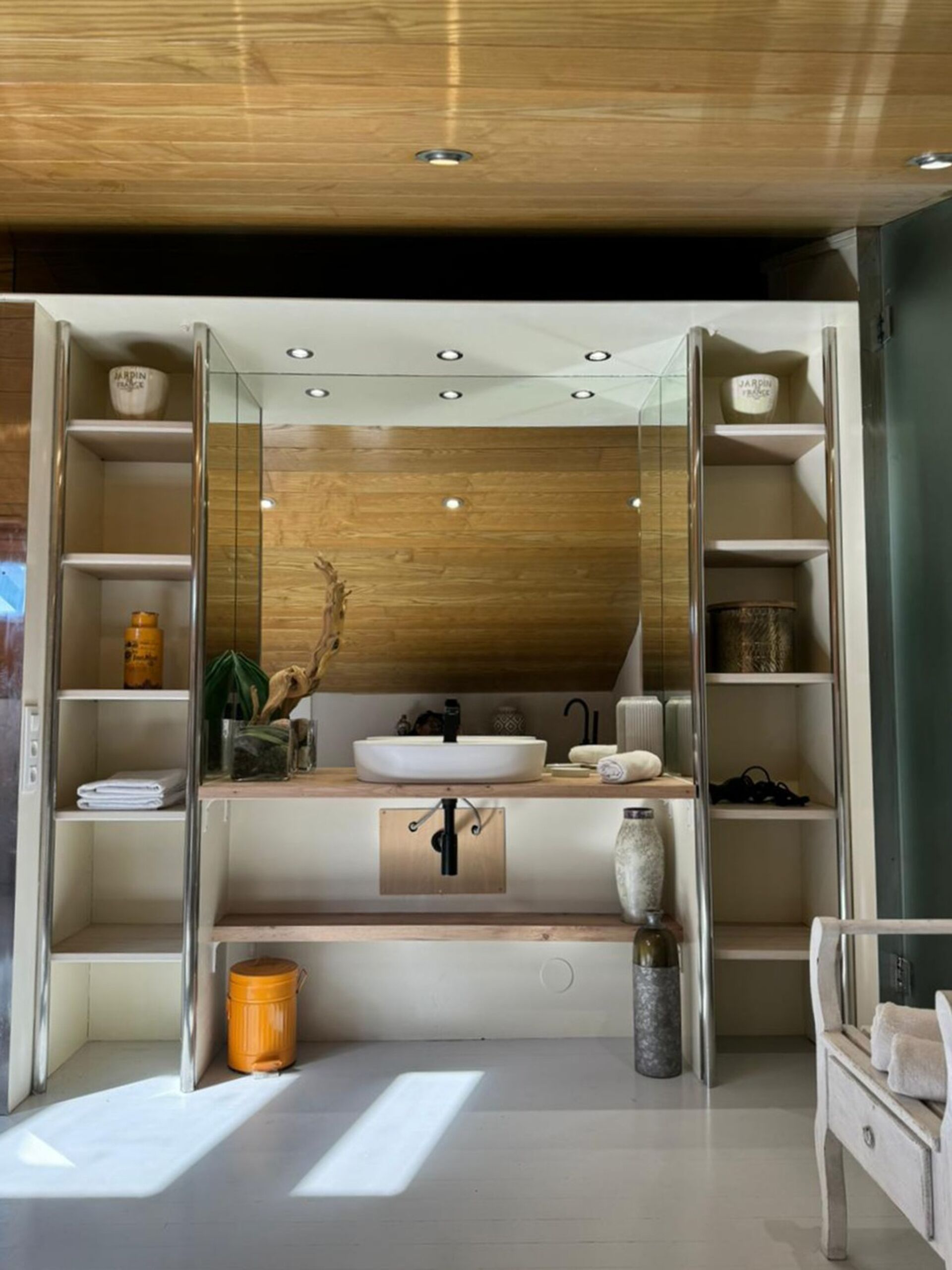 A modern bathroom with a wooden vanity, a large mirror, and built-in shelves.