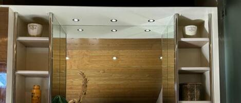 A modern bathroom with a wooden vanity, a large mirror, and built-in shelves.