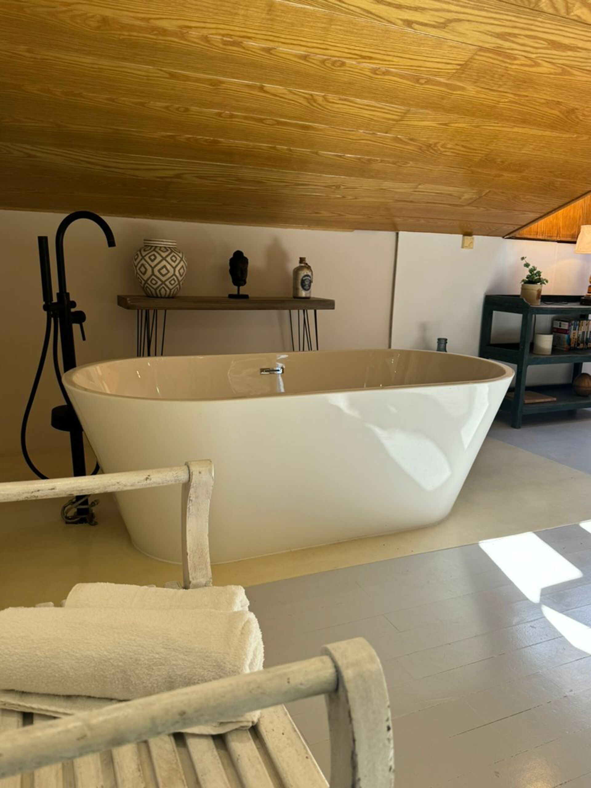 Una bañera grande independiente en una habitación con techo de madera y suelo de baldosas.