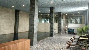 A lobby with a patterned ceiling, stone pillars, a reception desk, and a seating area with benches. - Pyramid Suites (Banjarmasin)