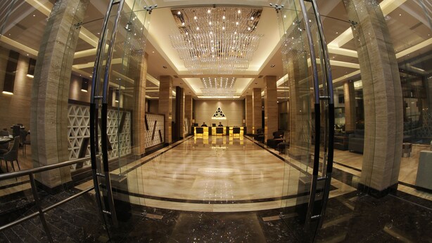 A spacious lobby with a reflective floor, a grand chandelier, and a reception desk in the center. - Pyramid Suites (Banjarmasin)