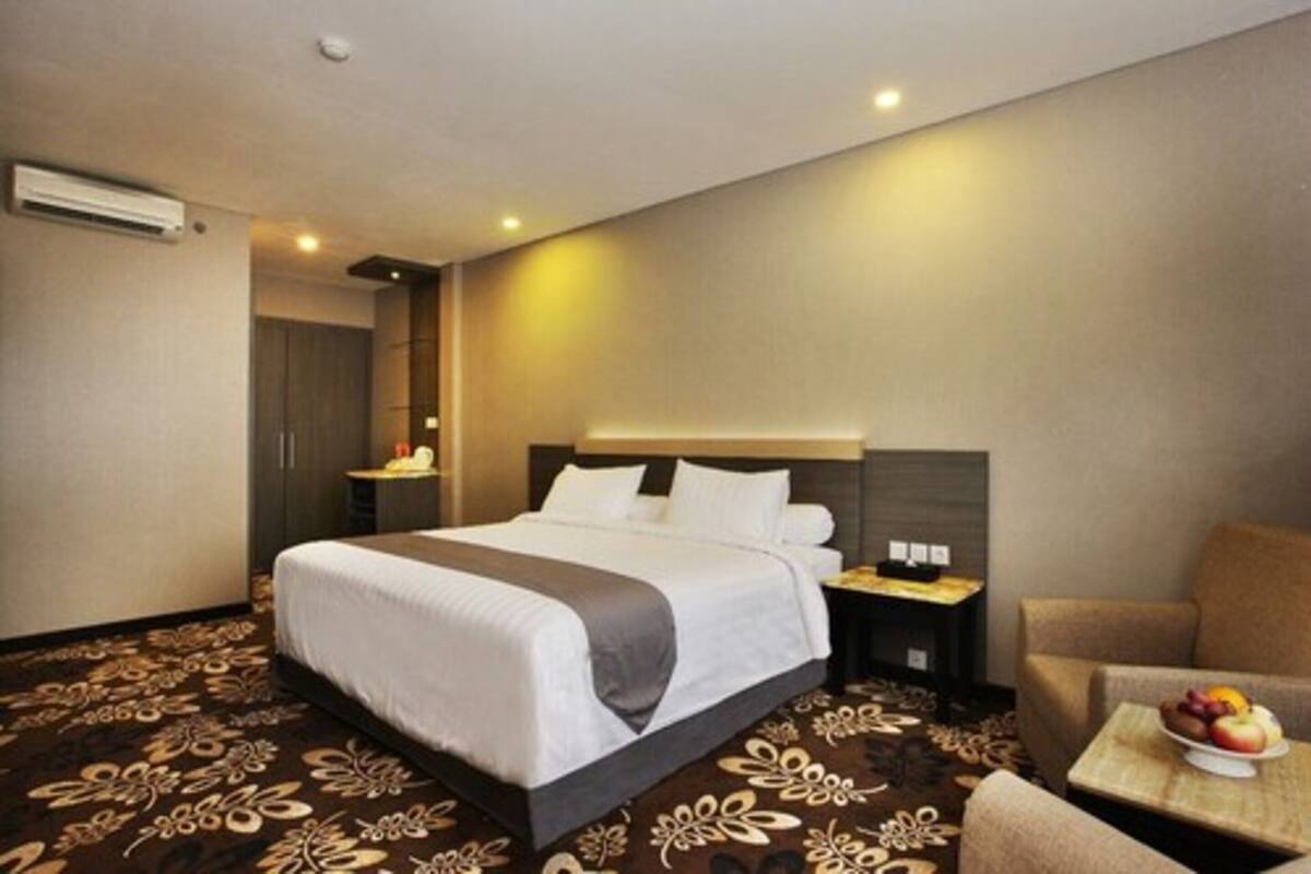 Ein Hotelzimmer mit einem großen Bett, einem Nachttisch mit Lampe, einem kleinen Tisch mit Obst und einem Sofa.