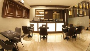 A modern kitchen with a central island, dark wooden cabinets, and a dining area with chairs and a table. - Pyramid Suites (Banjarmasin)