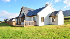 Une maison moderne avec un toit en pente, une terrasse en bois et une pelouse verdoyante.