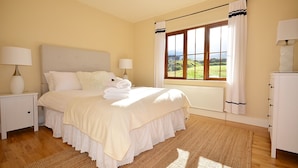 Une chambre à coucher bien rangée, avec un grand lit, deux lampes de chevet, une fenêtre avec des rideaux et un radiateur.