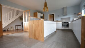 A modern kitchen with a central island, wooden staircase, and a hanging light fixture. - Sonas VRBO (Dingle)