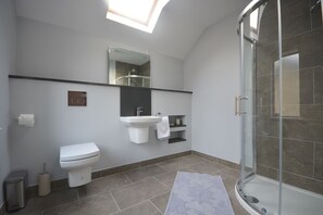Un baño moderno con tragaluz, inodoro, lavamanos, ducha y espejo.