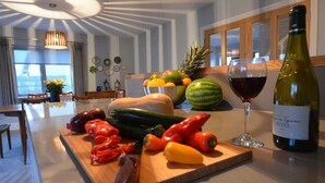 A kitchen counter with fresh vegetables, a bowl of fruit, a wine glass, and a bottle of wine. - Sonas VRBO (Dingle)