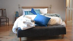 A bed with a wooden headboard, multiple pillows, and a blanket. A chair and a small table with a bottle and glasses are visible in the background. - Sonas VRBO (Dingle)