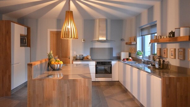 A modern kitchen with a central island, a hanging light fixture, and a window providing natural light. - Sonas VRBO (Dingle)