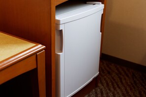 A compact white refrigerator in a wooden cabinet, a wooden table with a beige surface, and a carpeted floor. - Center Hotel Narita 1 (Narita)