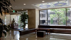 Eine Lobby mit Sitzgelegenheit, einer Statue und großen Fenstern mit Blick auf Gebäude und Bäume.