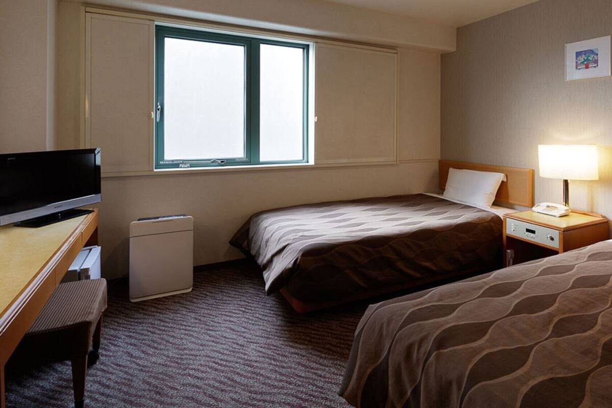 Een hotelkamer met twee bedden, een bureau met televisie, een klein nachtkastje met lamp en een raam.