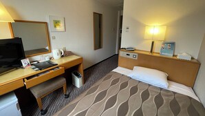 Ein Hotelzimmer mit einem Bett, einem Schreibtisch mit Computer, einem Telefon, einem Spiegel und einem Papierkorb.