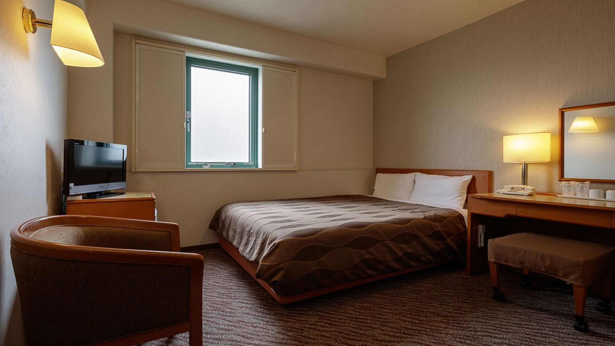 Ein Hotelzimmer mit Bett, Schreibtisch, Stuhl, Fernseher, Fenster und Lampe.