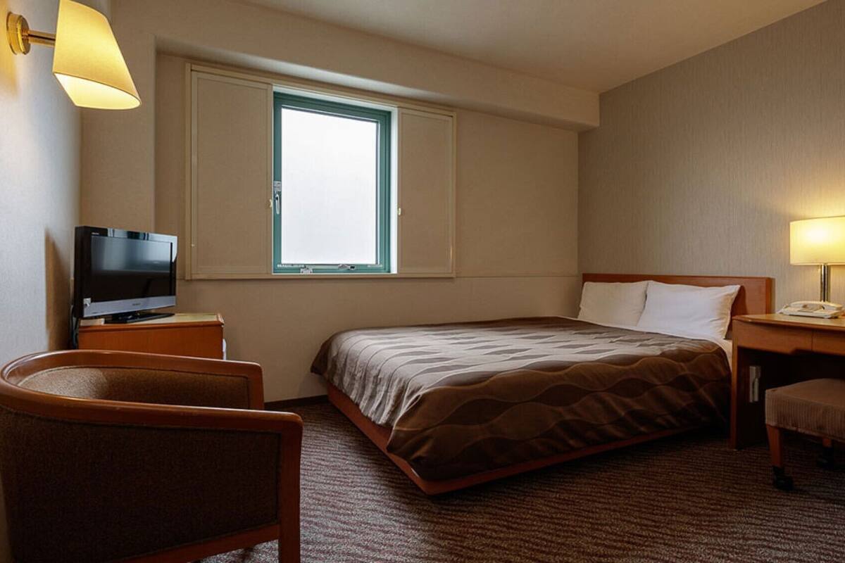 Hotelkamer met een bed, bureau, stoel, televisie, raam en lamp.