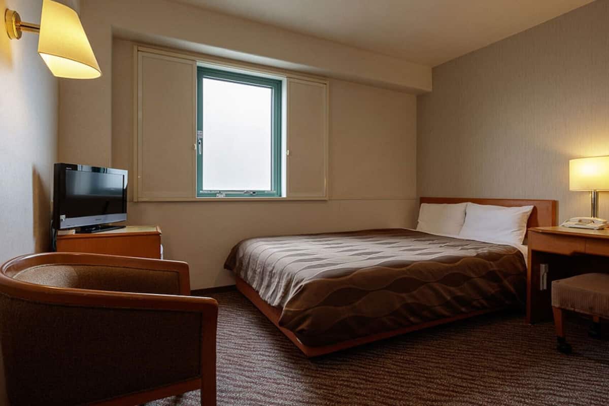 Une chambre d’hôtel équipée d’un lit, d’un bureau, d’une chaise, d’une télévision, d’une fenêtre et d’une lampe.