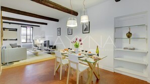 Ein modernes Wohnzimmer mit Essbereich, ausgestattet mit freiliegenden Holzbalken, einem Glastisch und weißen Möbeln.