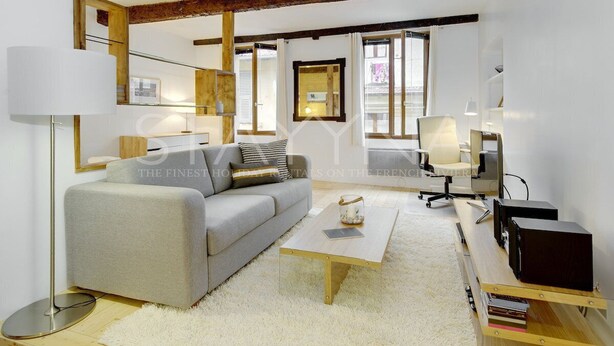 A modern living room with a grey sofa, a wooden coffee table, and a white rug. There is a desk with a computer and a lamp. - La Caravelle 1 bedroom apartment VRBO (Nice)