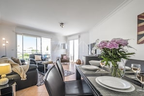 A modern living room with a dining area, large windows, and a view of the outdoors.