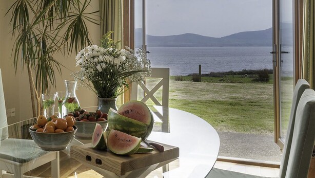 A dining table with a bowl of oranges, a watermelon, and a vase of flowers. - The Lookout 3 bedroom house (Dingle Peninsula)