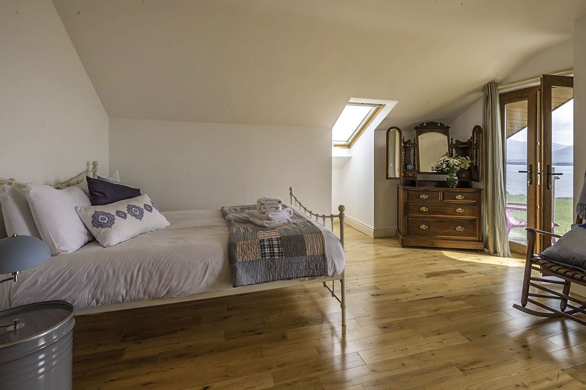 A bedroom with a bed, wooden dresser, and a view of a body of water through a door.