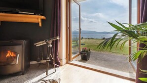 A living room with a fireplace, a television, and a large window with a view of the sea. - The Lookout 3 bedroom house (Dingle Peninsula)