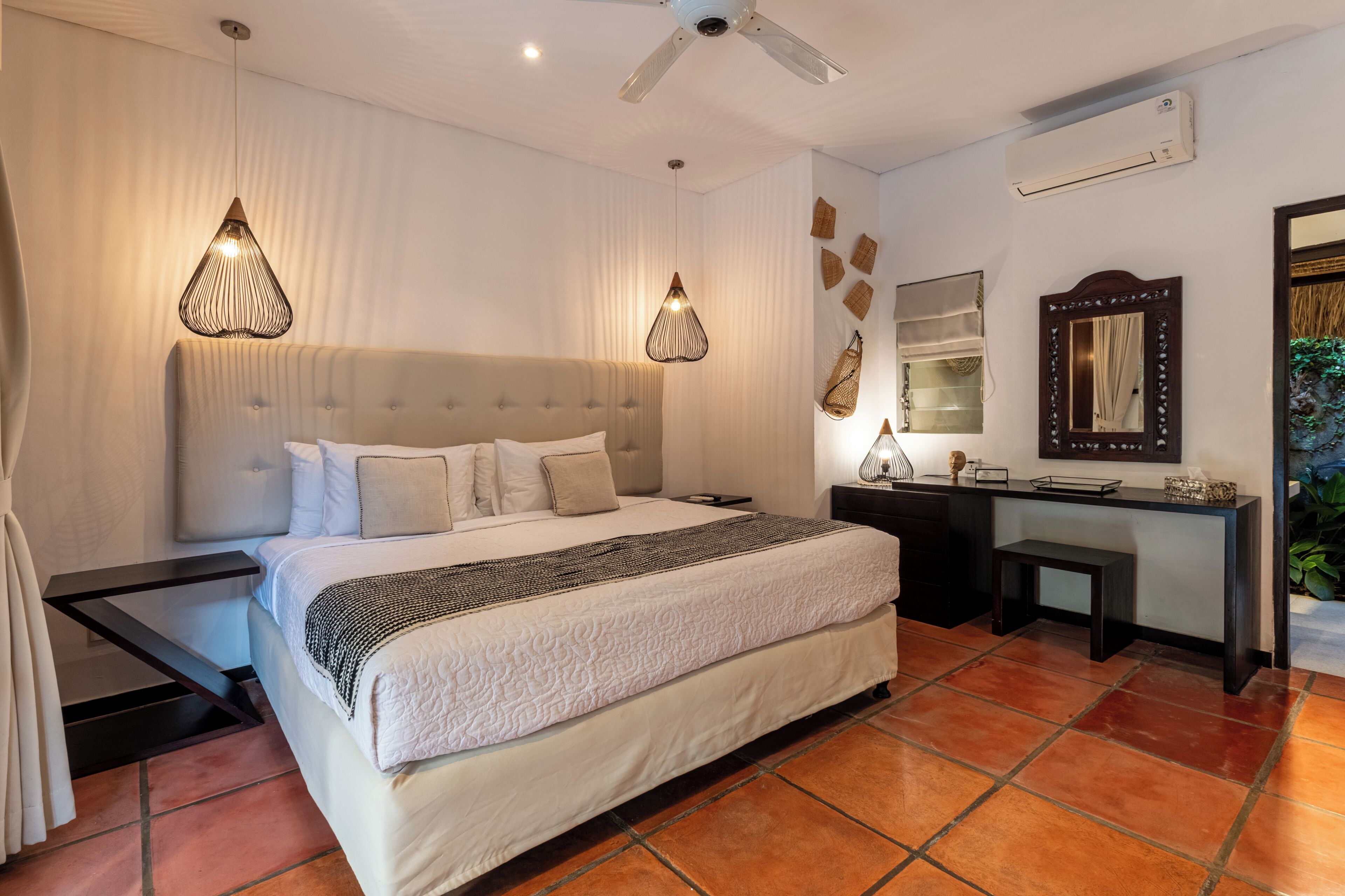 Une chambre d’hôtel avec un grand lit, un bureau, une chaise, un ventilateur de plafond et un appareil de climatisation.