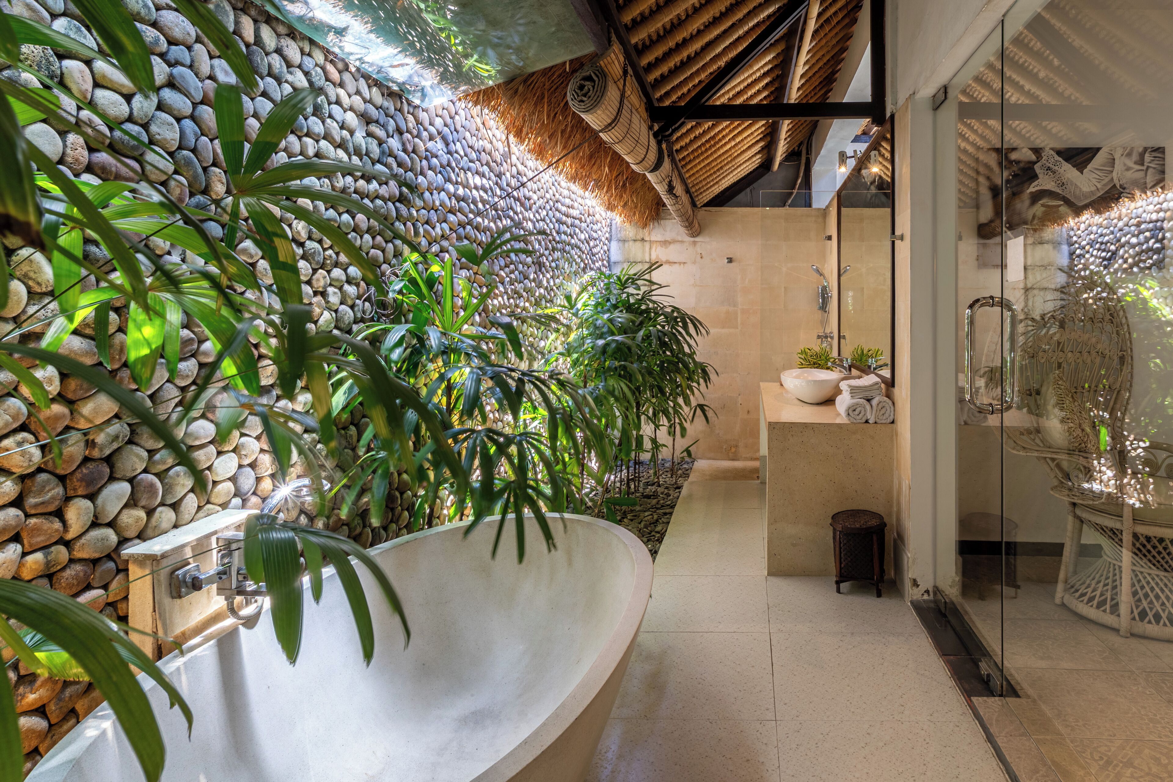 Ein Badezimmer mit einer Steinswand, einer großzügigen Badewanne und unterschiedlichen Pflanzen.
