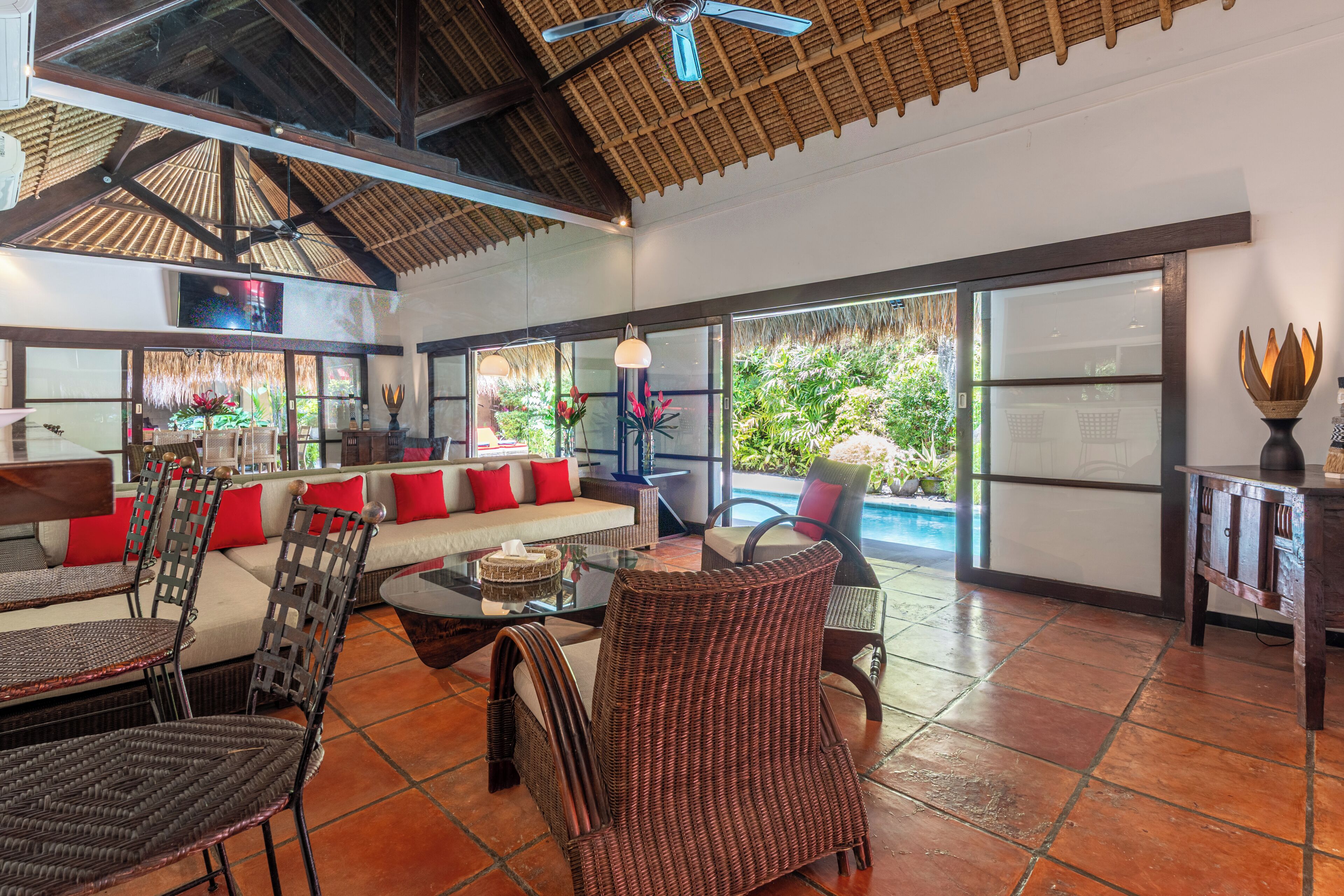 A spacious living area with a large glass door leading to a pool, a ceiling fan, and a seating area with wicker furniture.