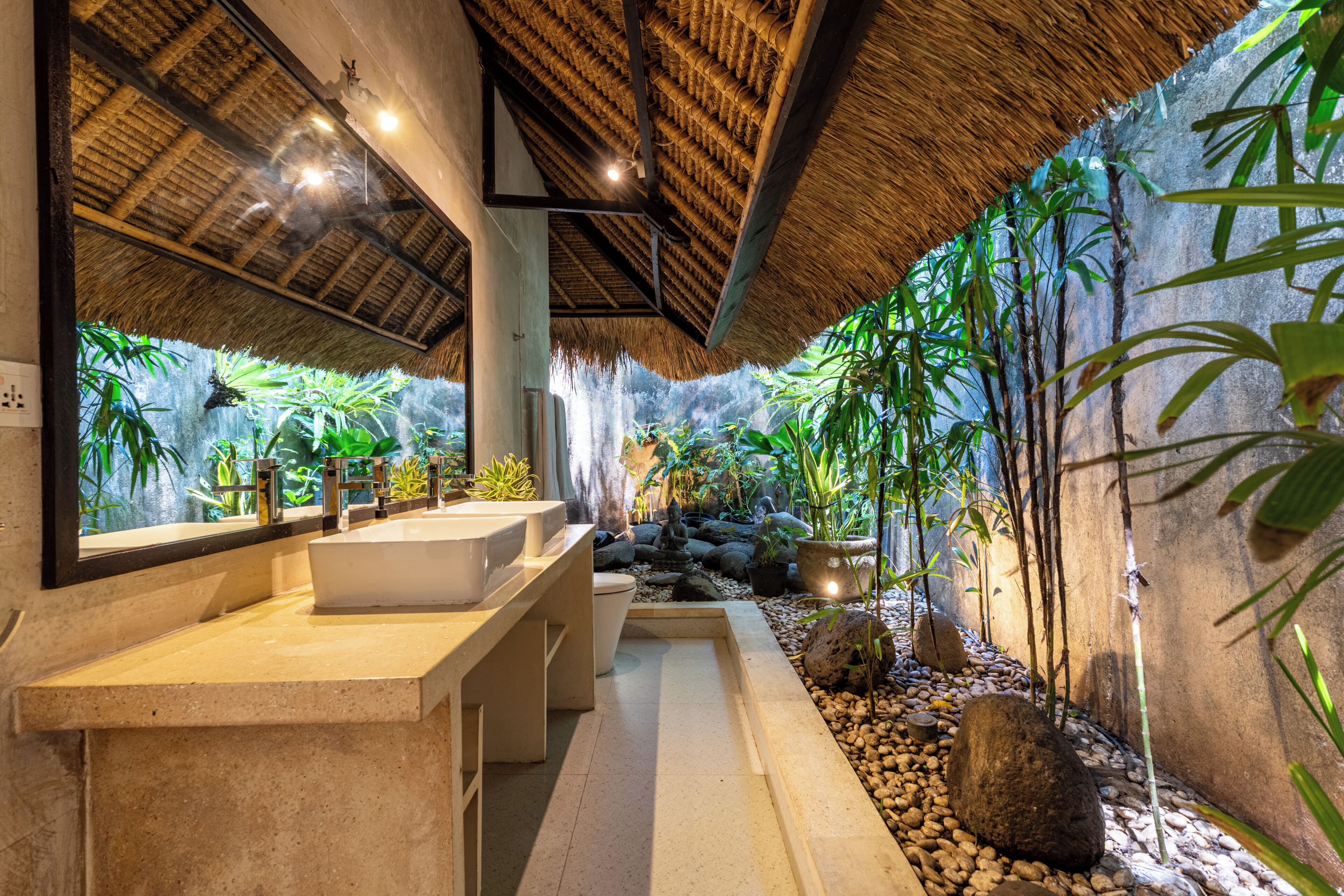 A bathroom with a large mirror, a bathtub, and a sink. There are plants and rocks around the room.