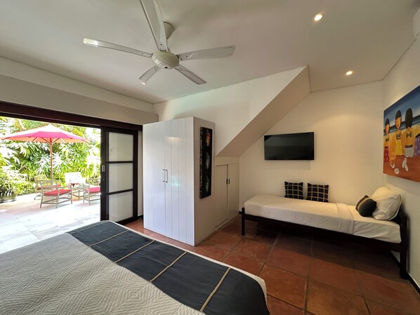 A bedroom with a bed, a sofa, a wardrobe, a ceiling fan, a TV, and a painting.