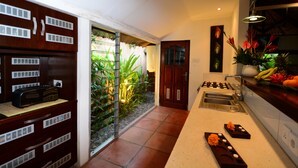 A modern kitchen with a gas stove, sink, and a small dining area with a table and chairs. - Villa Elleo (Seminyak)