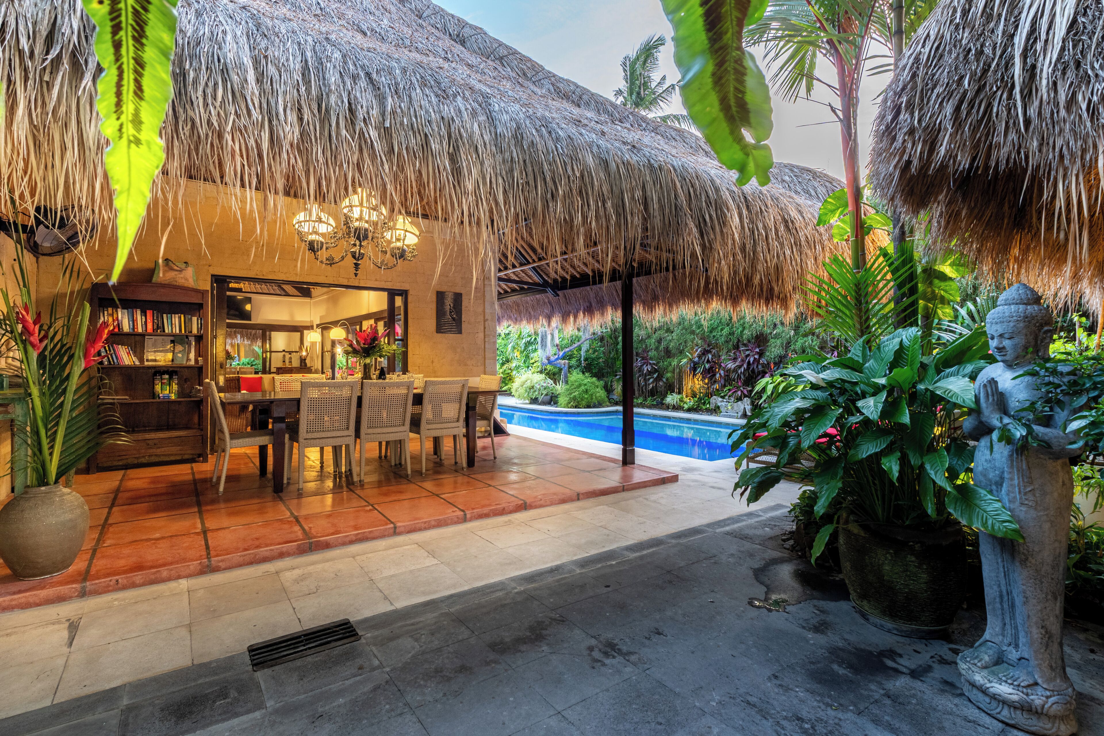 A restaurant with a thatched roof, indoor seating, and a pool area.