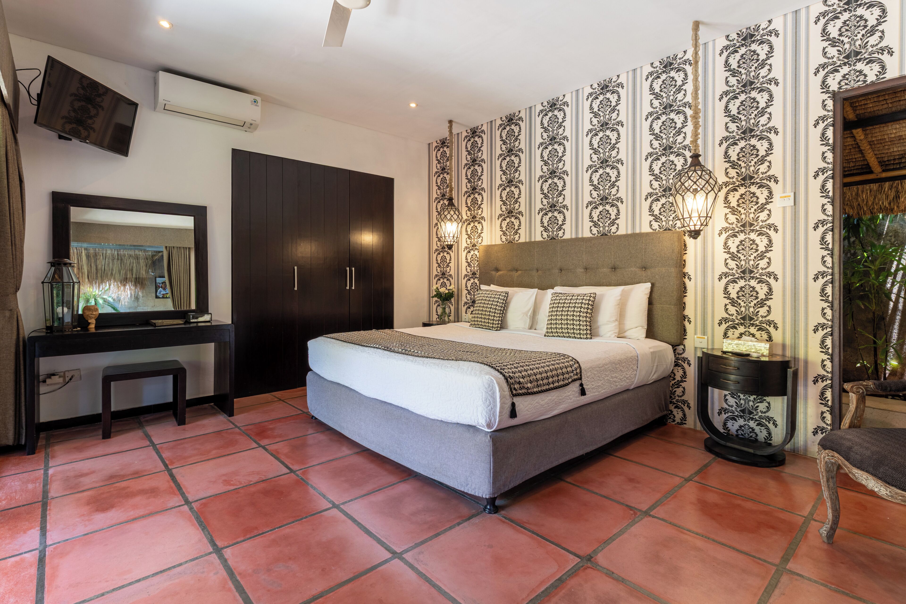A bedroom with a bed, a desk, a wardrobe, and patterned wallpaper.
