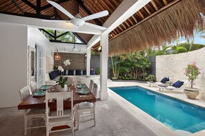Ein Essbereich mit Blick auf den Pool, ausgestattet mit einem Holztisch, weißen Stühlen und einem Deckenventilator.