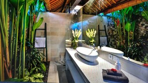 A modern bathroom with a large mirror, two sinks, and a stone wall. - Villa Elleo (Seminyak)