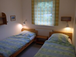 Une petite chambre simple, avec deux lits simples, une fenêtre donnant sur un paysage agréable et un radiateur.