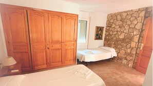 Un dormitori amb dos llits, un armari de fusta, una paret de pedra i un quadre a la paret.