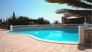 Una piscina amb tanca blanca, parets de pedra i terrassa amb rajoles.