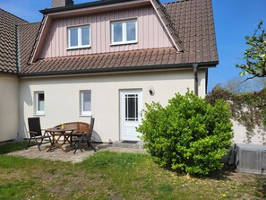 Une maison à deux étages, avec un toit en tuiles, une porte d’entrée et un petit patio aménagé avec du mobilier d’extérieur.
