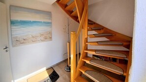 Eine Holztreppe mit strukturierter Teppichauflage, ein Gemälde mit Strandmotiv und eine Tür mit Fußmatte.