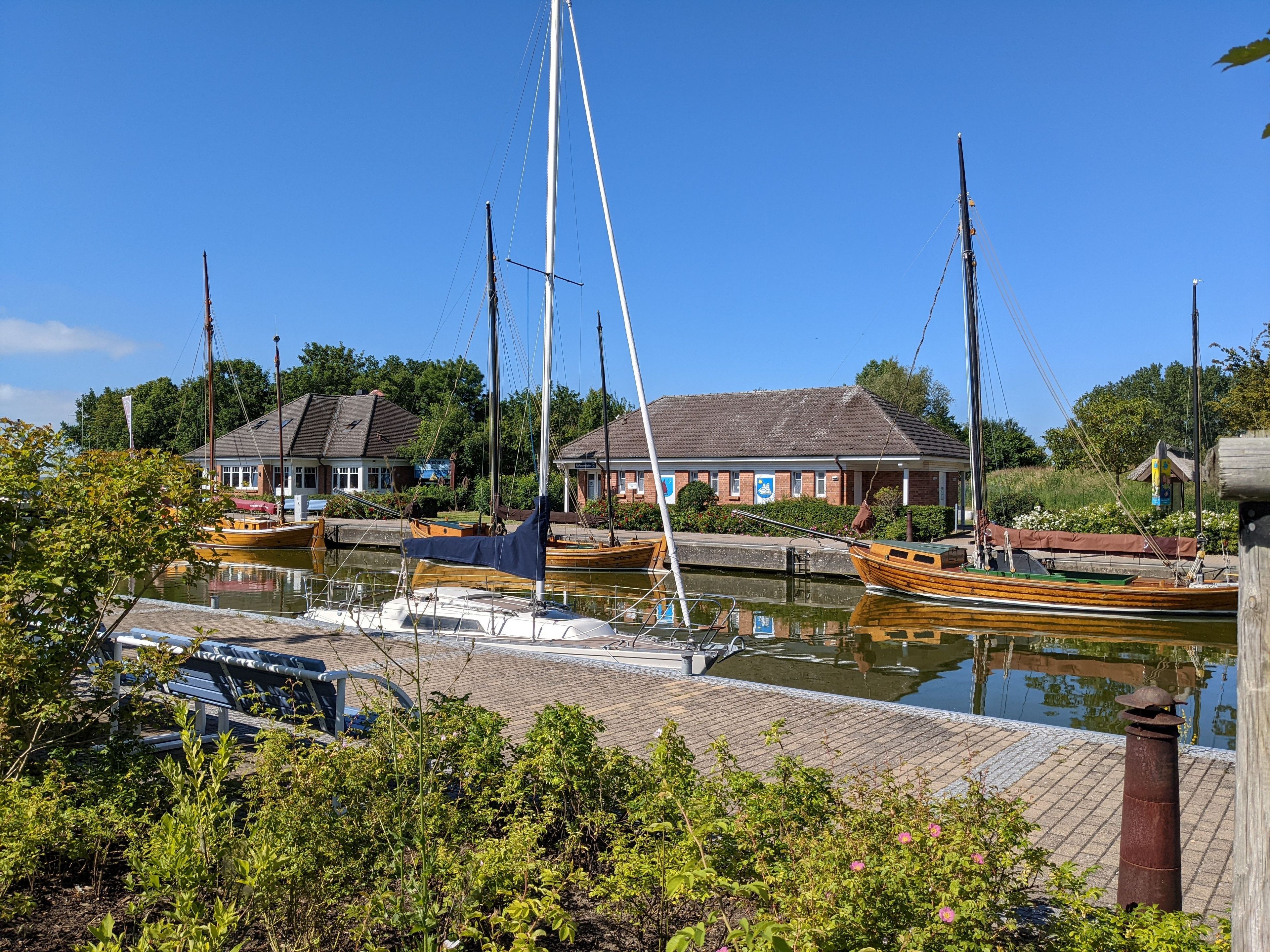 Ein Hafen mit vertäuten Booten, ein Backsteinhaus und Grünpflanzen im Vordergrund.
